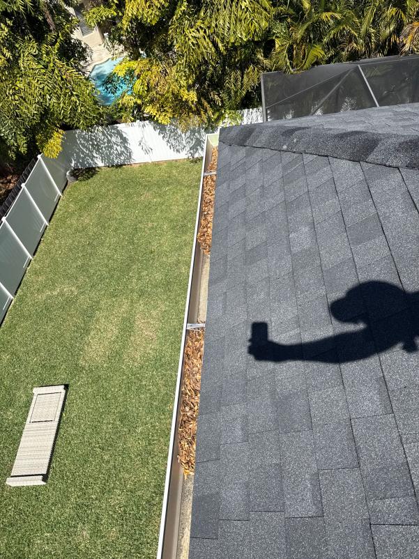 Gutter Cleaning Service Showing Debris Along The Edge Of A Roof With A Shadow Of A Person Holding A Phone